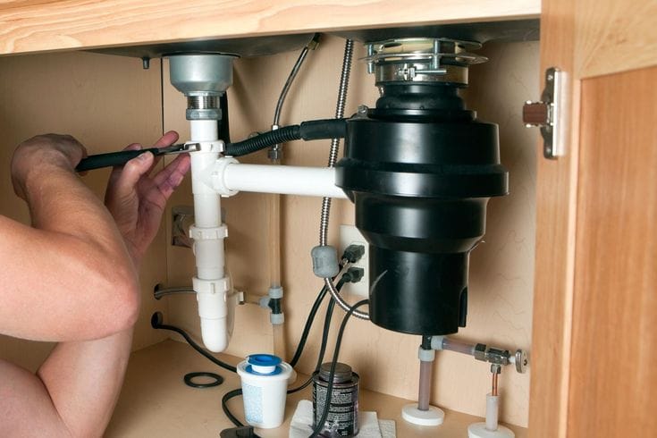 Plumber installing a garbage disposal beneath a kitchen sink in Smyrna