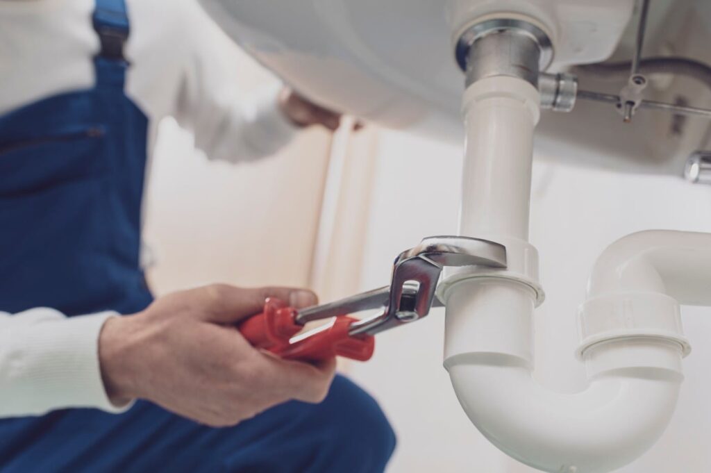 Plumber repairing a white drain pipe beneath a sink in Smyrna